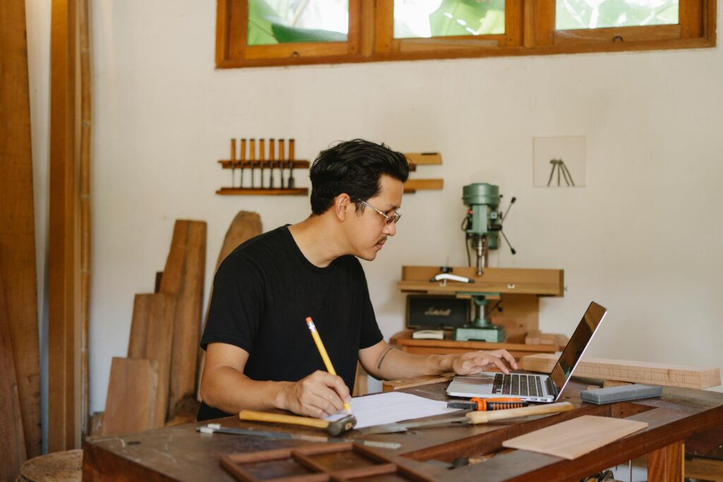 A dedicated carpenter designing a woodworking project on a laptop in his workshop.